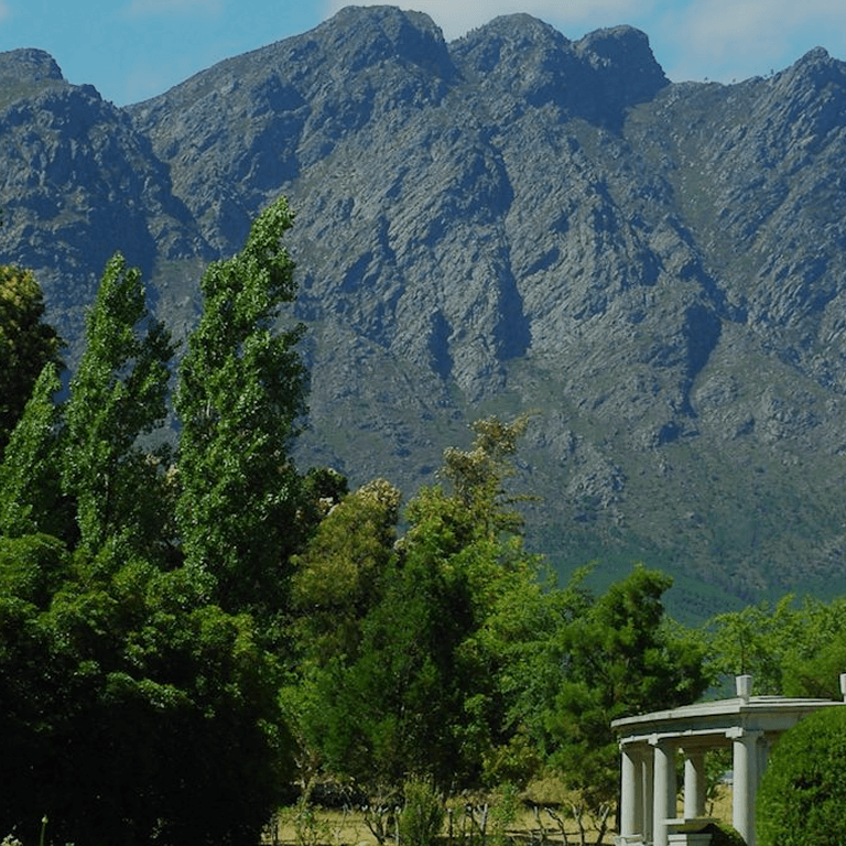 Jardín con árboles, montañas y un monumento bajo un cielo azul.