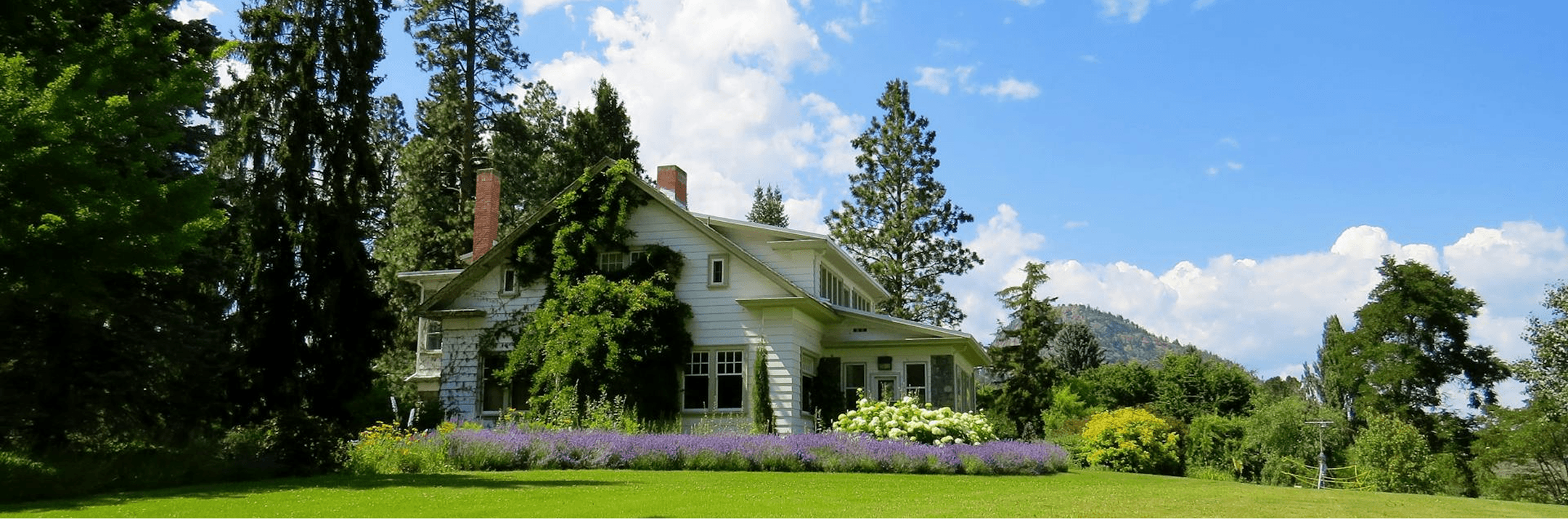 Casa rural rodeada de árboles y jardín con montañas al fondo