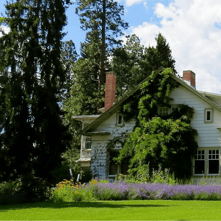 Casa rural rodeada de árboles y jardín con montañas al fondo